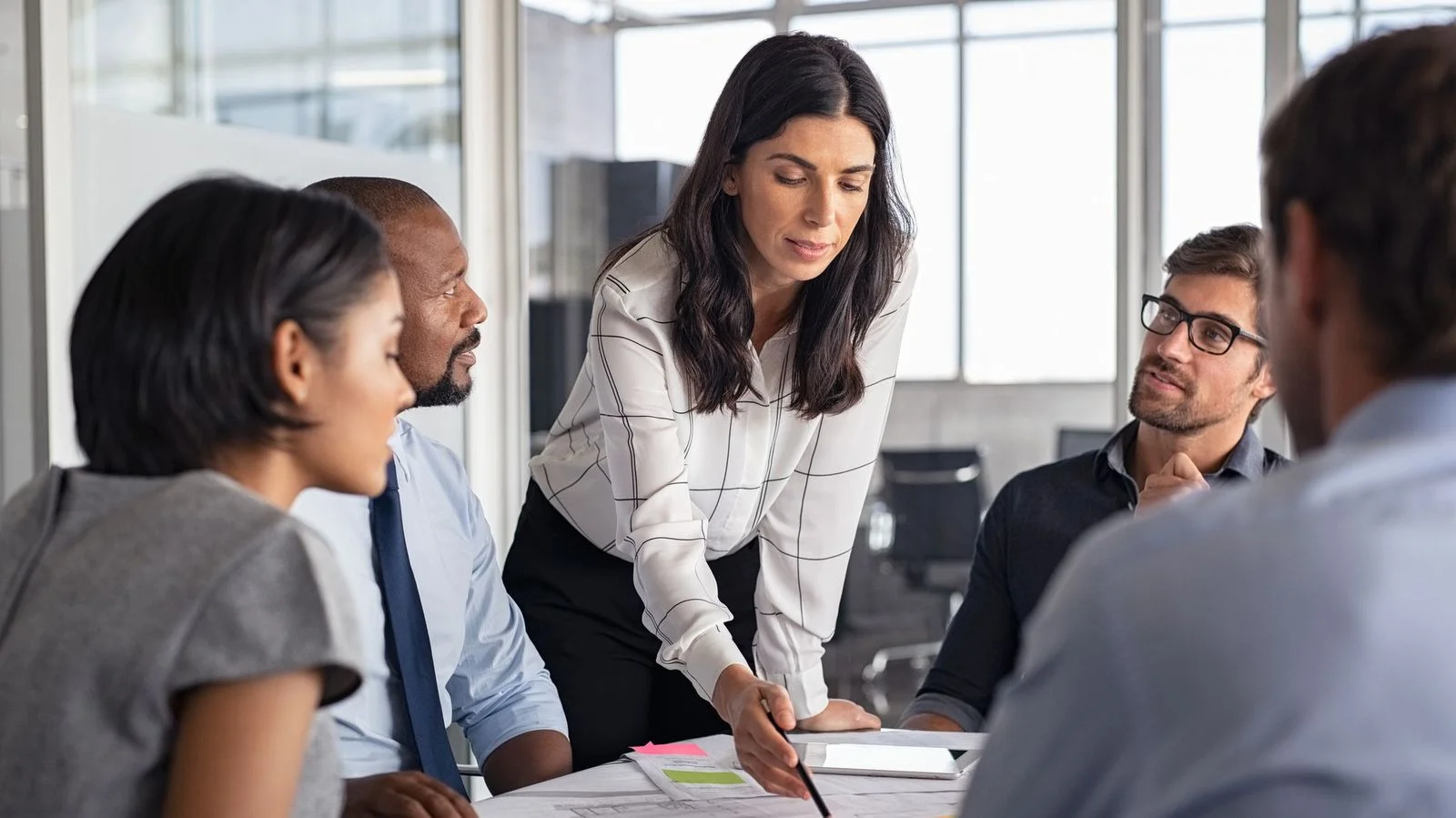 Uma mulher chefe planejando com sua equipe sobre uma mesa, discutindo negócios e próximos passos.